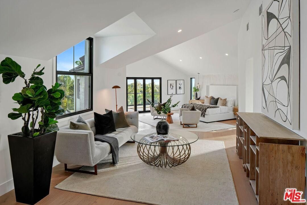Bright modern living room with vaulted white ceiling, gray chairs, wood console, and large windows