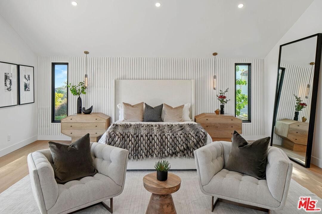 Bright modern bedroom with a bed, two armchairs, wood accents, and large windows