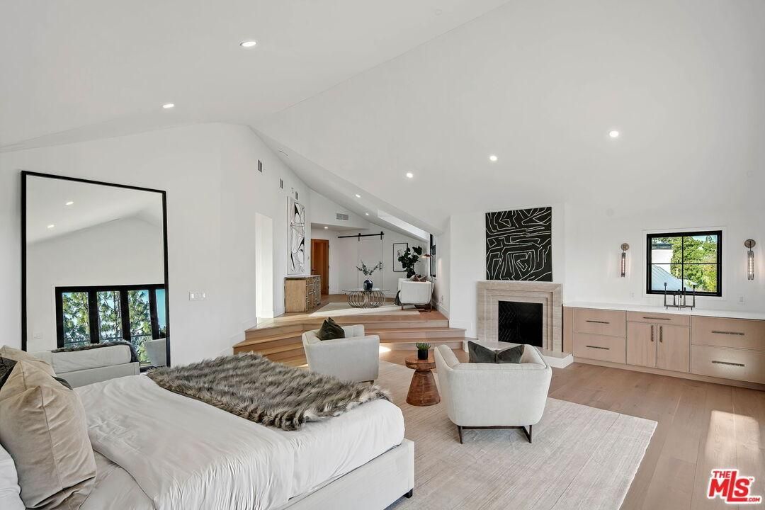 Bright white open-plan living room with fireplace, large mirror, steps, and modern wood cabinetry.