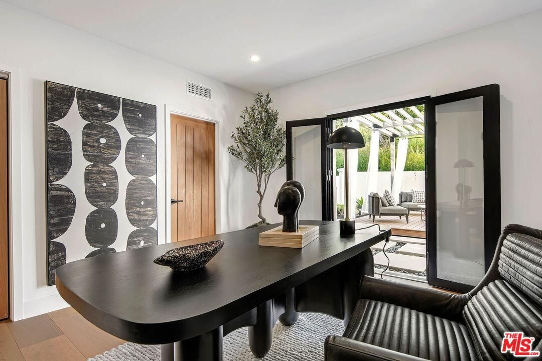 Modern home office with a black desk, patterned chairs, and open glass doors to a patio.