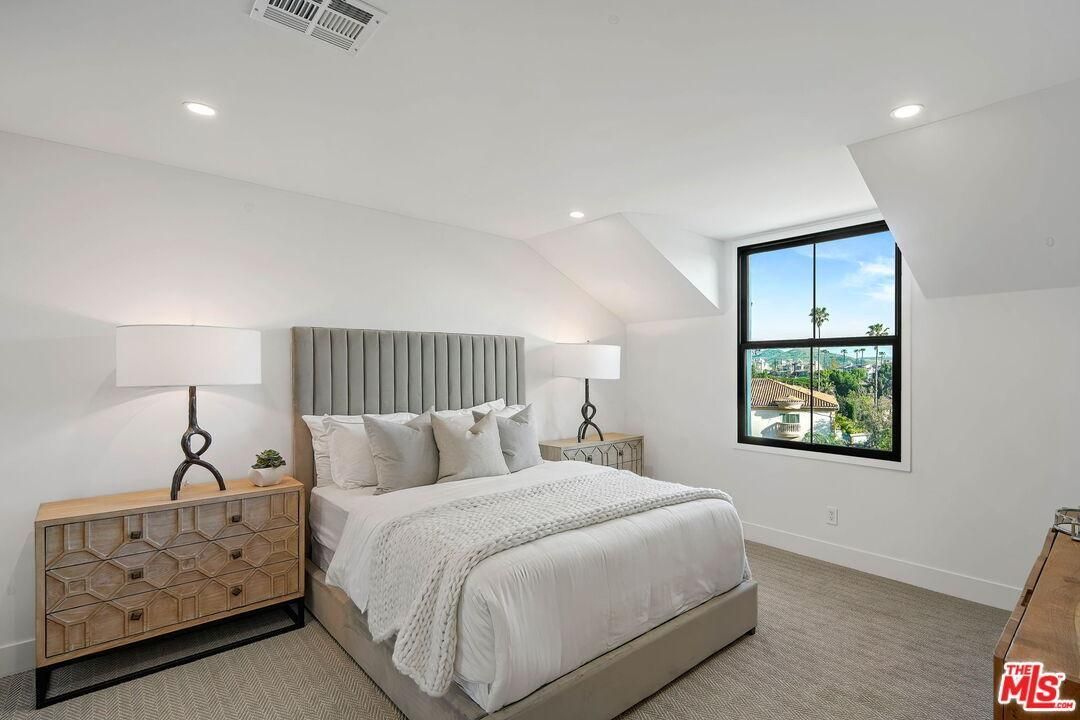 Bright bedroom with a bed, bedside lamps, and a window showing greenery.