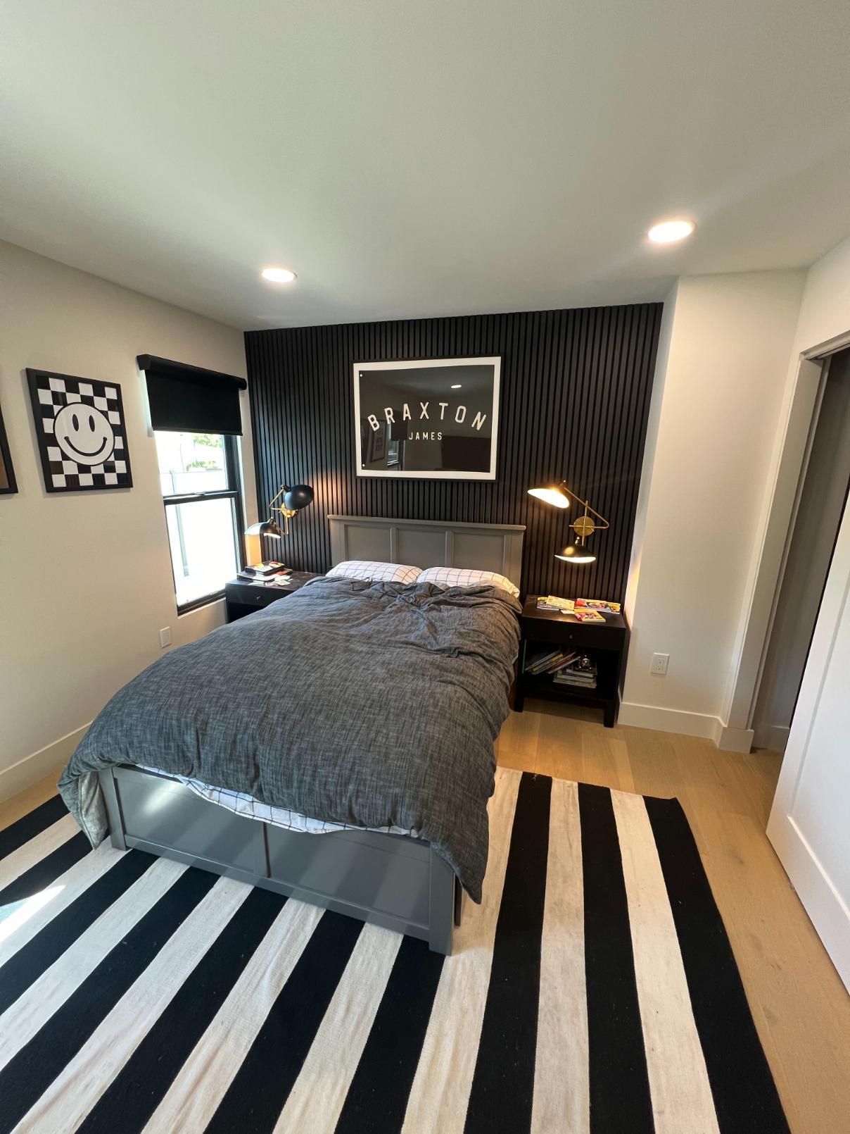 Modern bedroom with black accent wall, gray bed, striped black-and-white rug, and bedside lamps