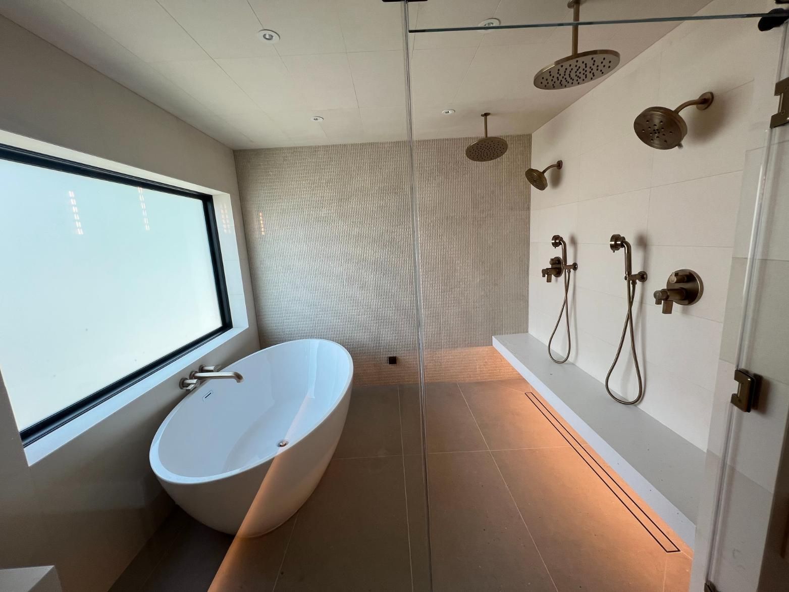 Modern bathroom with a freestanding tub, large frosted window, and wall-mounted shower fixtures