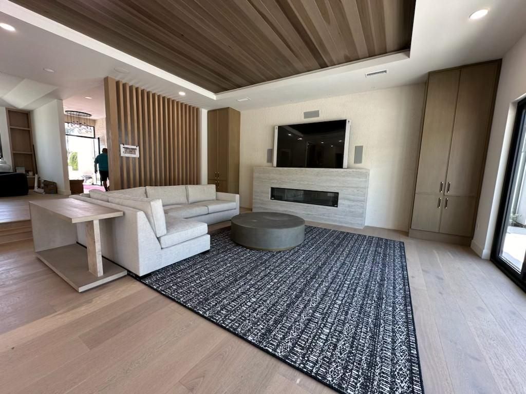 Modern living room with white sofa, patterned rug, round ottoman, and built-in fireplace under wood ceiling