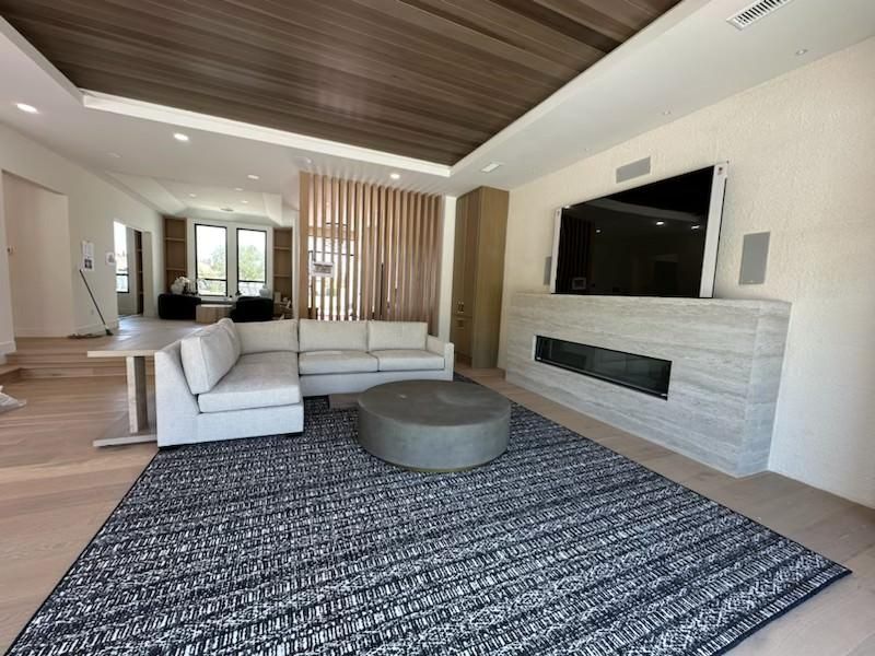 Modern living room with gray sectional, round ottoman, patterned rug, wood ceiling, and wall-mounted TV
