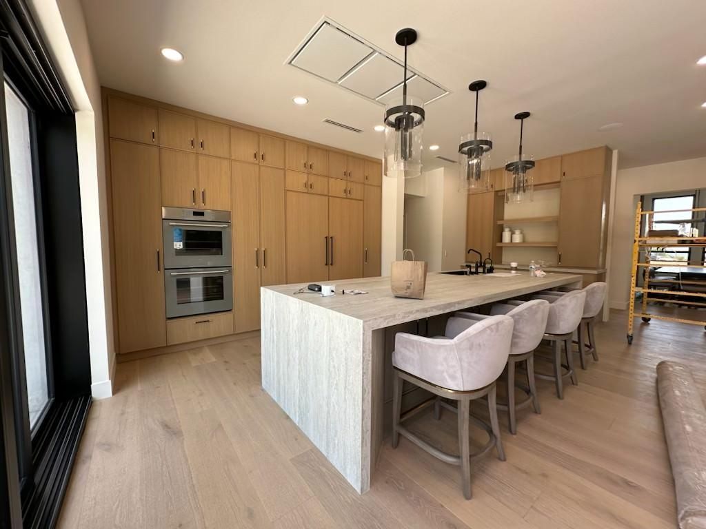 Modern kitchen with light wood cabinets, marble island, and pendant lights.