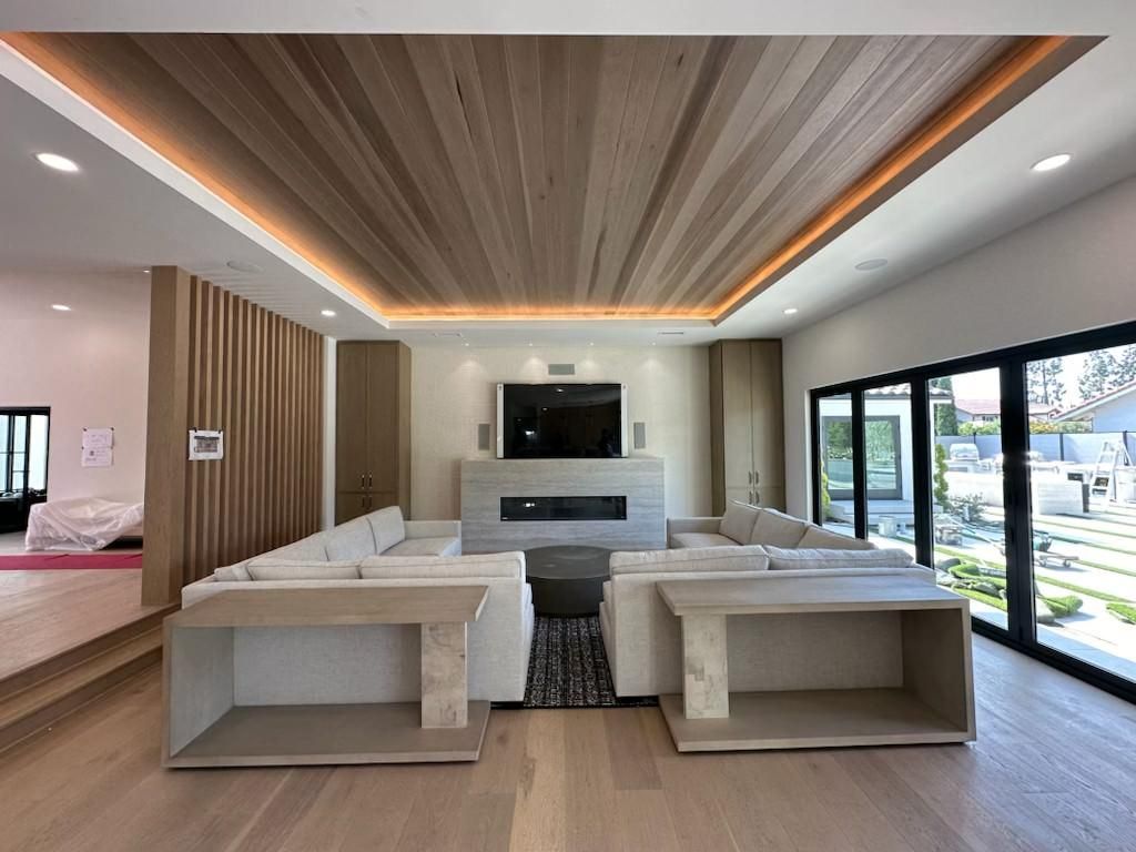 Modern living room with beige sofas, wall TV, wood ceiling, and large windows overlooking a patio.