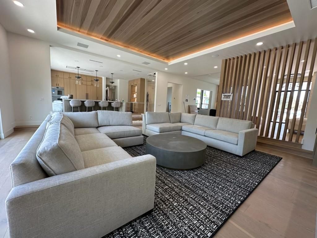 Modern lounge with light gray sectional sofas, round coffee table, and wood slat partition under a recessed ceiling