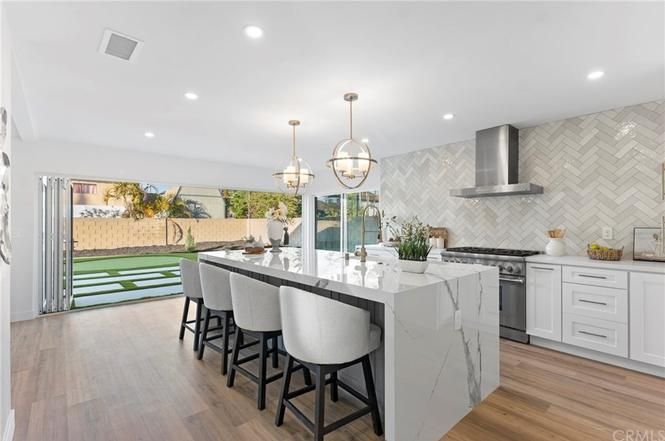 Bright modern kitchen with white cabinets, marble island, and open doors to a patio and pool