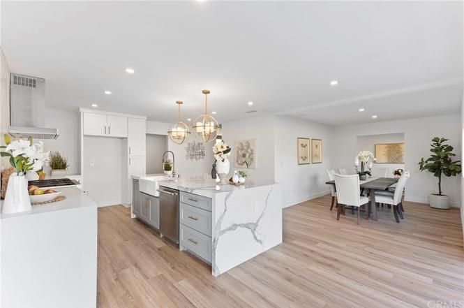 Bright open-concept kitchen and dining area with white cabinets, marble island, and light wood floors