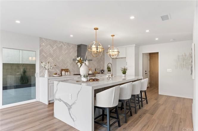 Bright modern kitchen with white marble island, gold pendant lights, and wood floors
