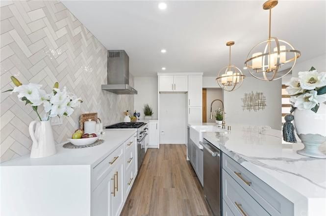 Bright modern kitchen with white cabinetry, marble counters, gold pendant lights, and wood flooring