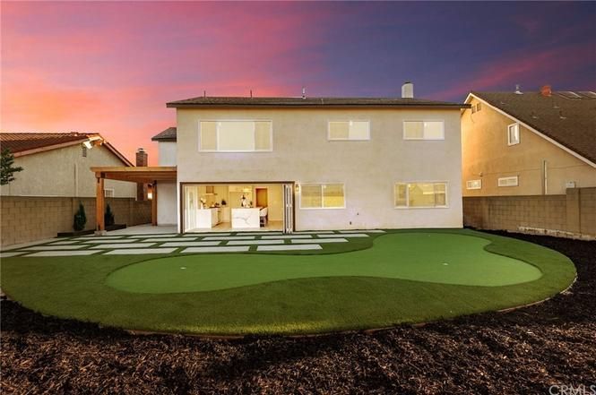 Backyard view of a two-story house with a patio and bright green artificial lawn at sunset