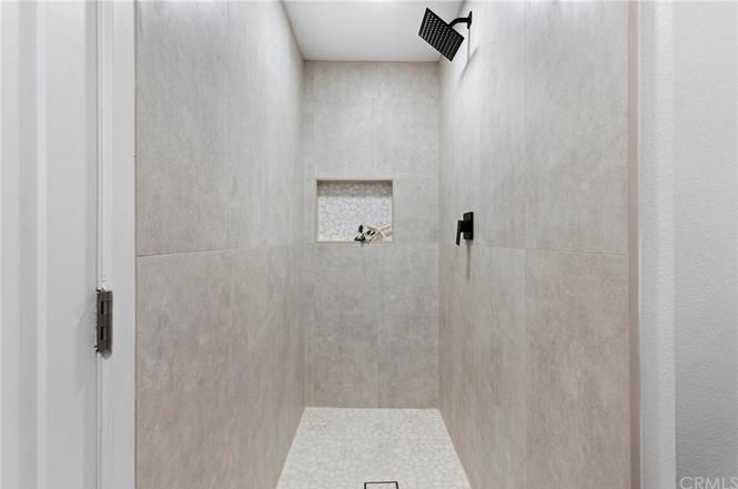 Modern tiled walk-in shower with two black fixtures and a small window at the far end