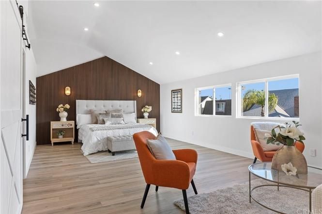 Bright modern bedroom with slanted ceiling, white bed, orange chair, wood accent wall, and large windows