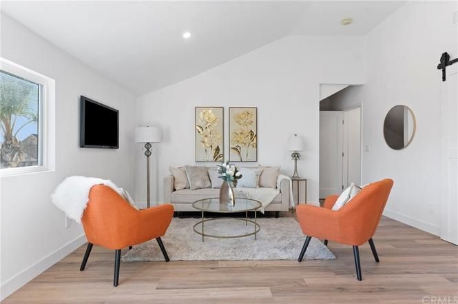 Bright living room with orange chairs, beige sofa, wall-mounted TV, and round coffee table