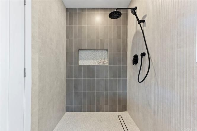 Modern walk-in shower with gray tile, rainfall head, handheld sprayer, and built-in niche
