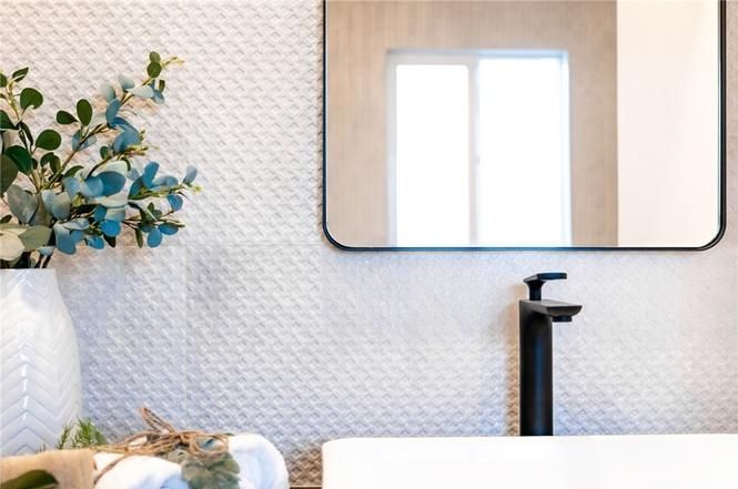 Modern bathroom vanity with black faucet, mirror, and vase of greenery on a patterned wall