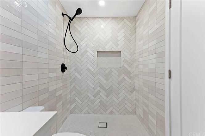Empty tiled shower with herringbone walls, black shower fixtures, and a recessed niche.