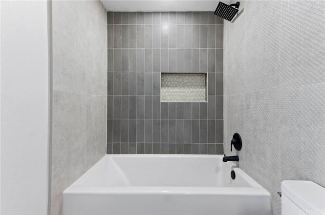 Modern white bathroom with a bathtub, gray tiled shower wall, and wall-mounted showerhead