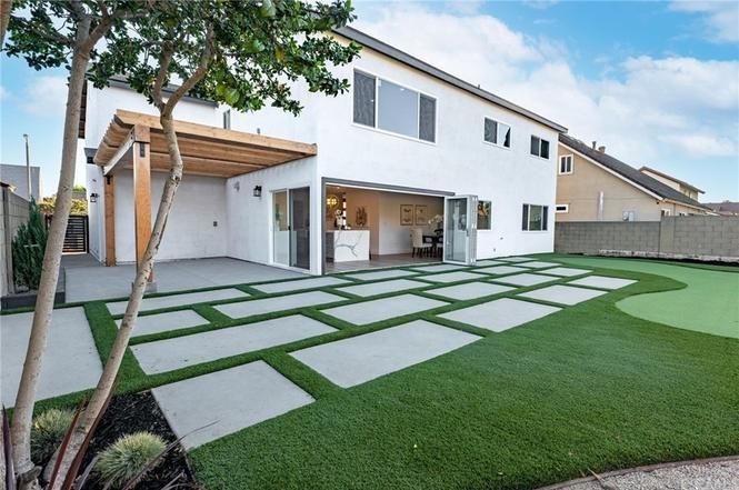 Modern white two-story house with patio, stone paver walkway, and green lawn