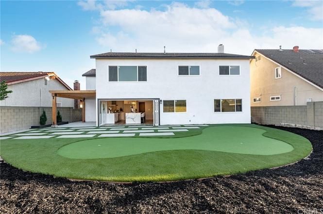 Backyard with modern two-story house, patio, and landscaped lawn.