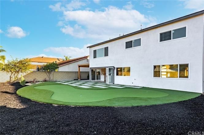 Backyard with a two-story white house and a large green lawn under a blue sky