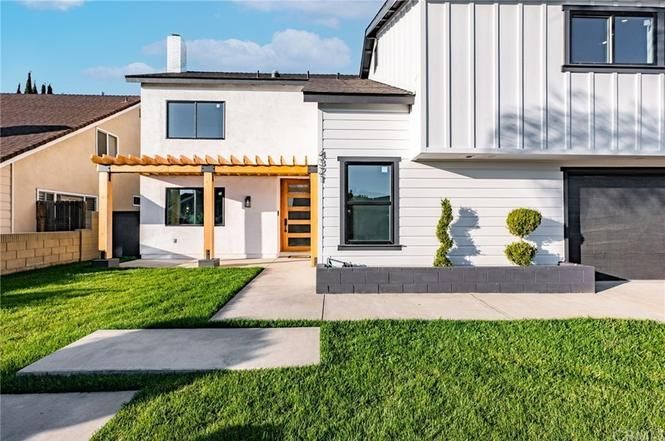 Modern white two-story house with a green lawn, walkway, and small landscaped shrubs