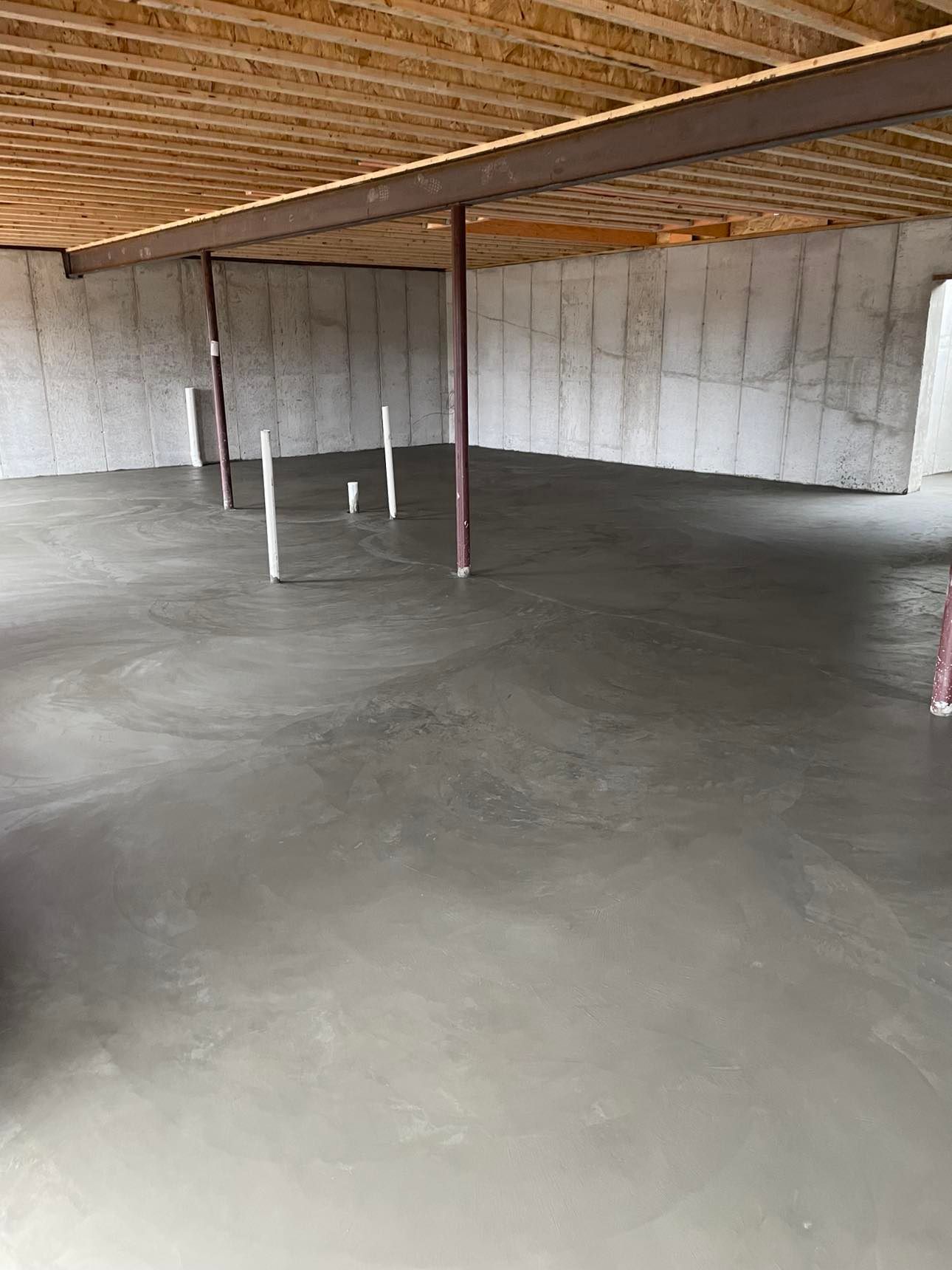 Empty concrete basement with white cinderblock walls, exposed wood ceiling, and support posts.