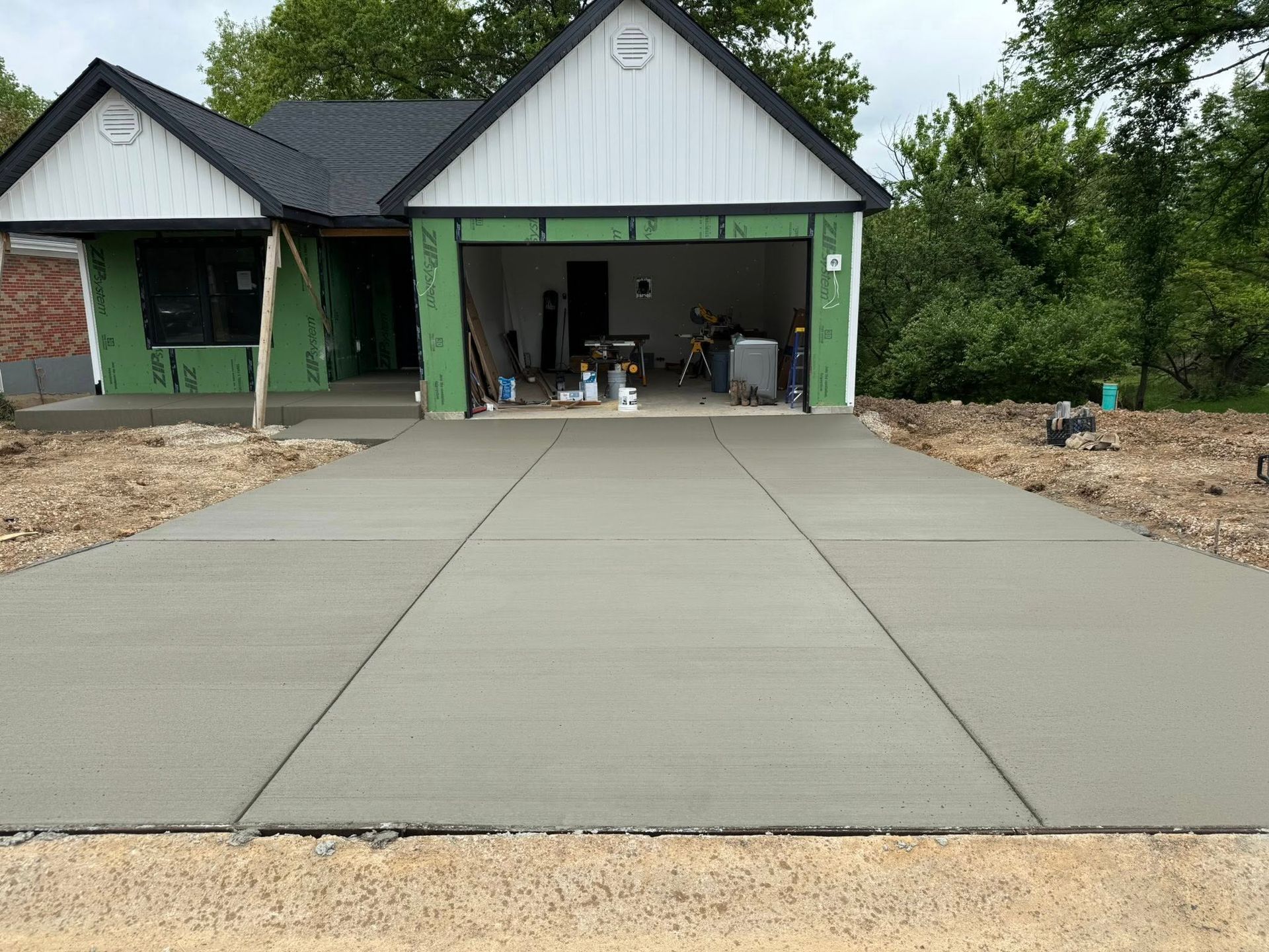 Concrete driveway leading to a green-trimmed house with open garage under construction