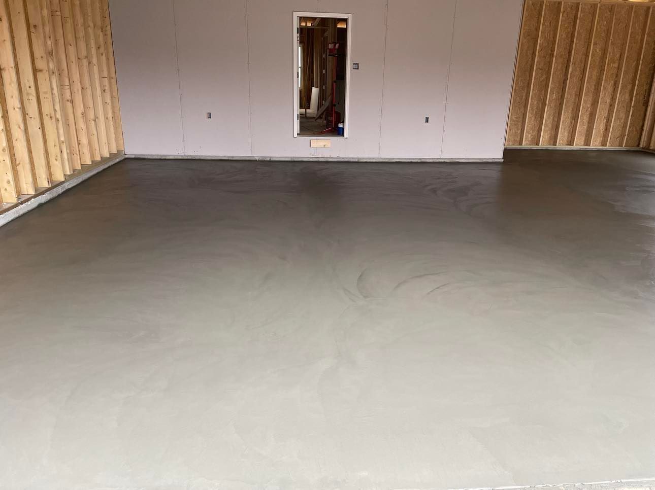Empty unfinished room with smooth gray concrete floor and exposed wood framing along the walls.