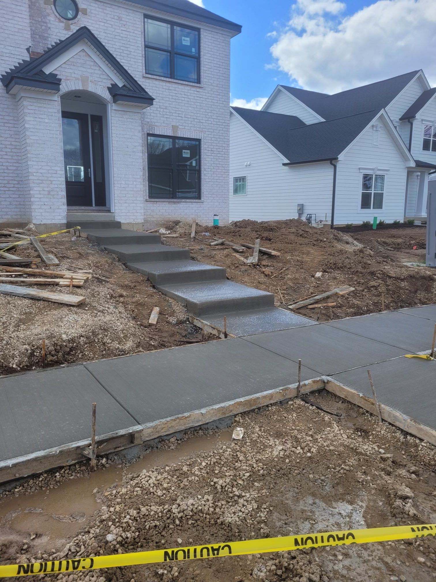 New house under construction with front steps, bare dirt yard, and sidewalk in the foreground