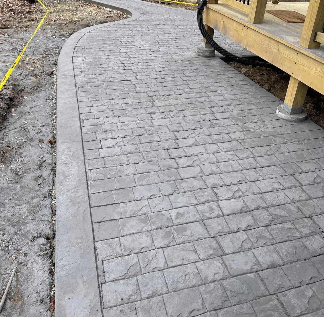 Curved gray brick walkway beside a wooden structure and muddy ground