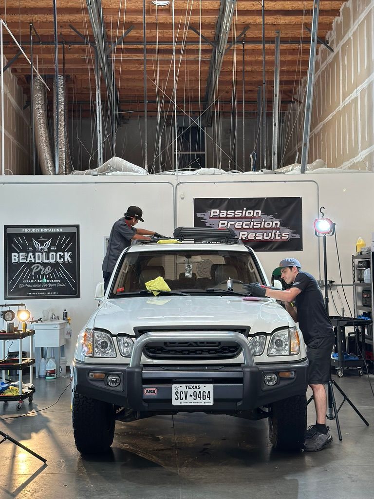 Two men cleaning a white SUV in a workshop. A banner reads 