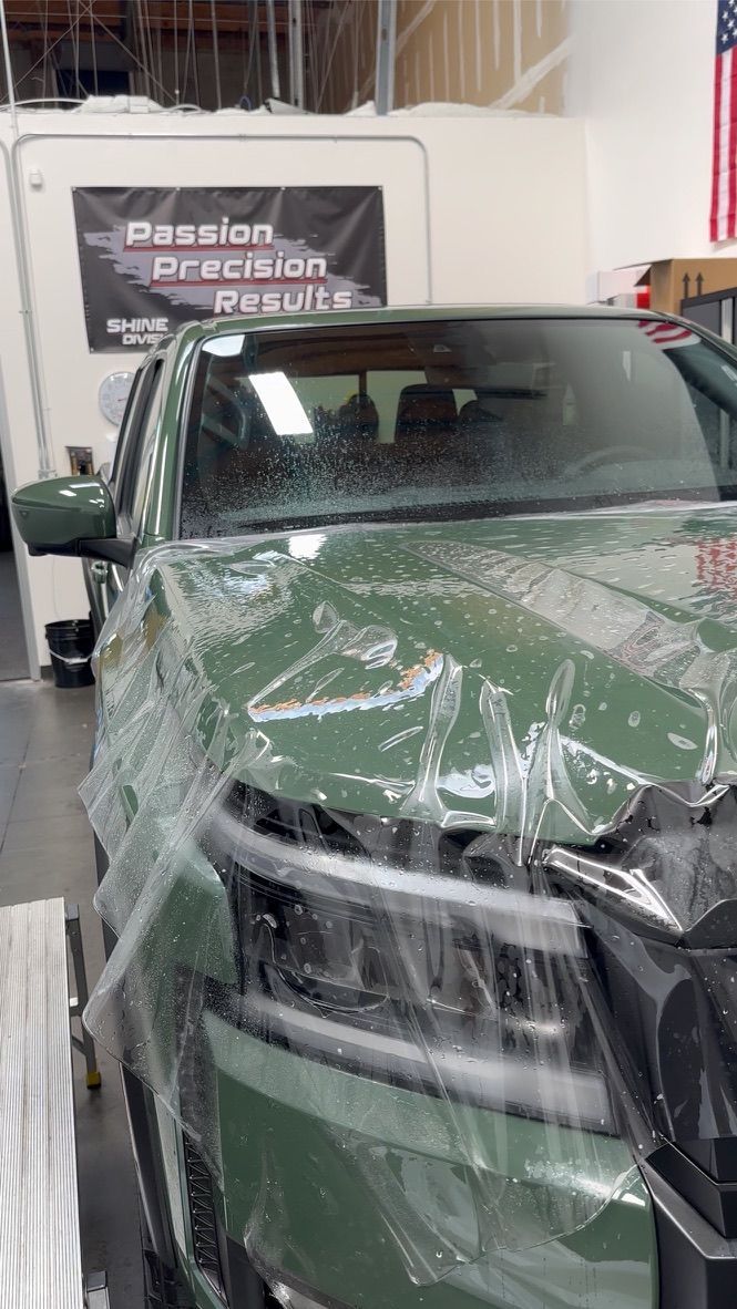 Green car covered in clear protective film in a shop; applying paint protection film.