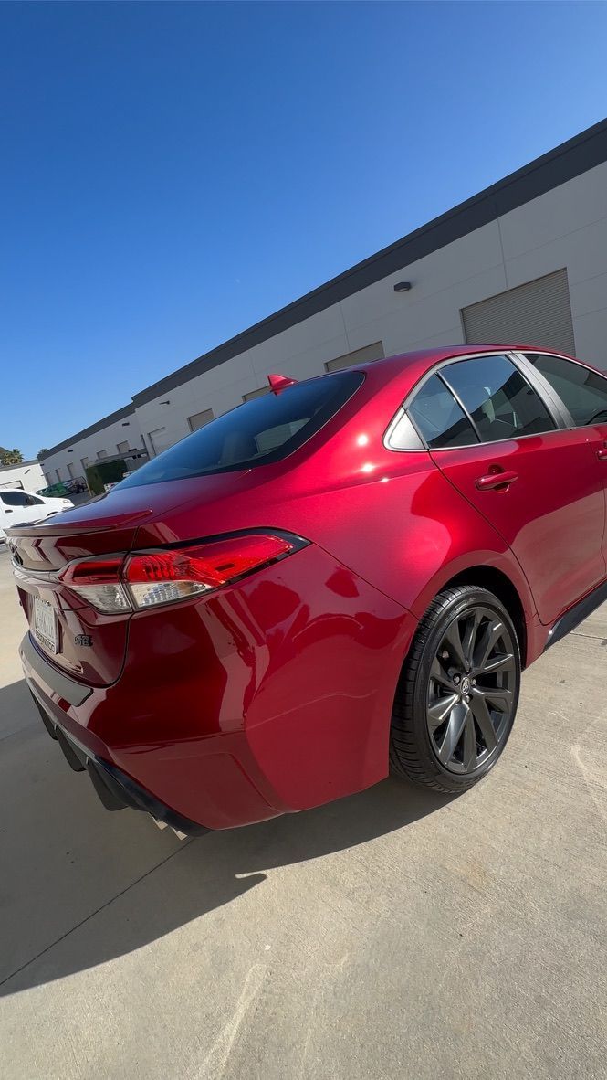 Red Toyota Corolla sedan parked on pavement under a clear blue sky.