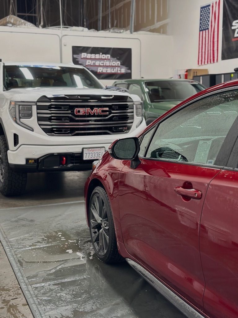 Red car being washed in a garage, with a white GMC truck in the background.