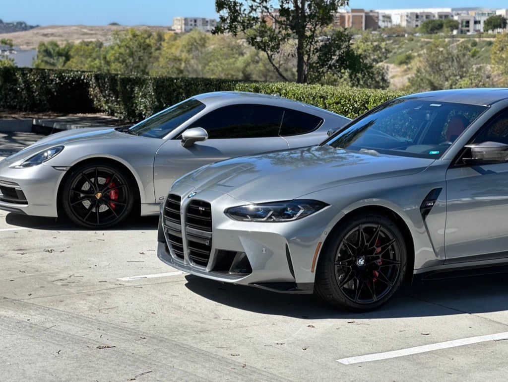 Silver Porsche and BMW parked side-by-side on a sunny day.