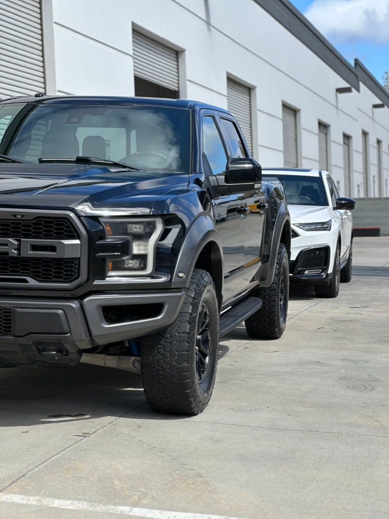 Black Ford Raptor truck parked next to a white SUV in front of a building.
