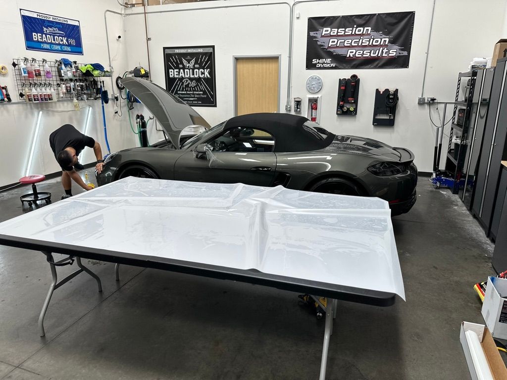 Man working on a gray convertible car in a garage with a folding table covered in white plastic.