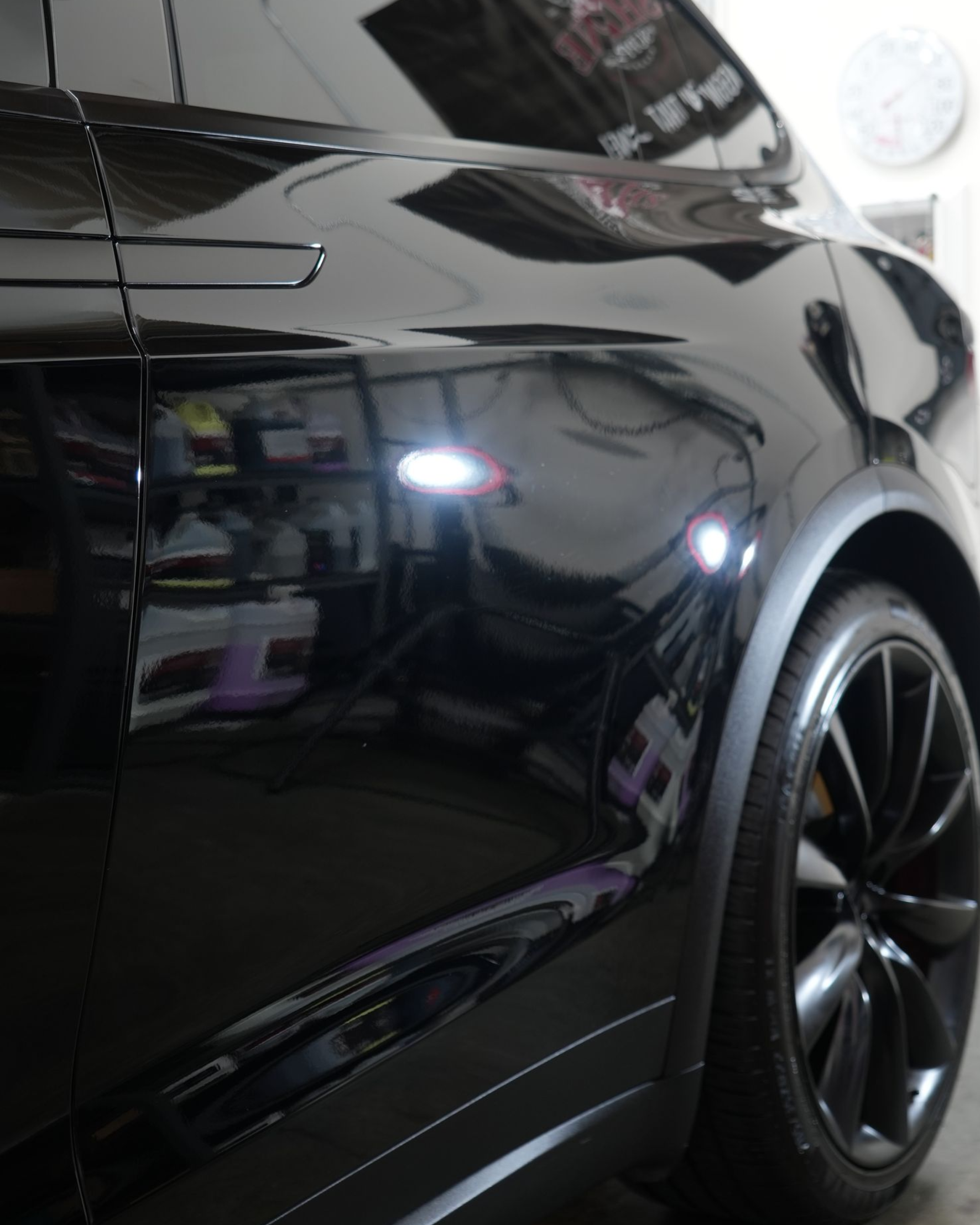 Glossy black sedan parked indoors, close-up on rear side and wheel.