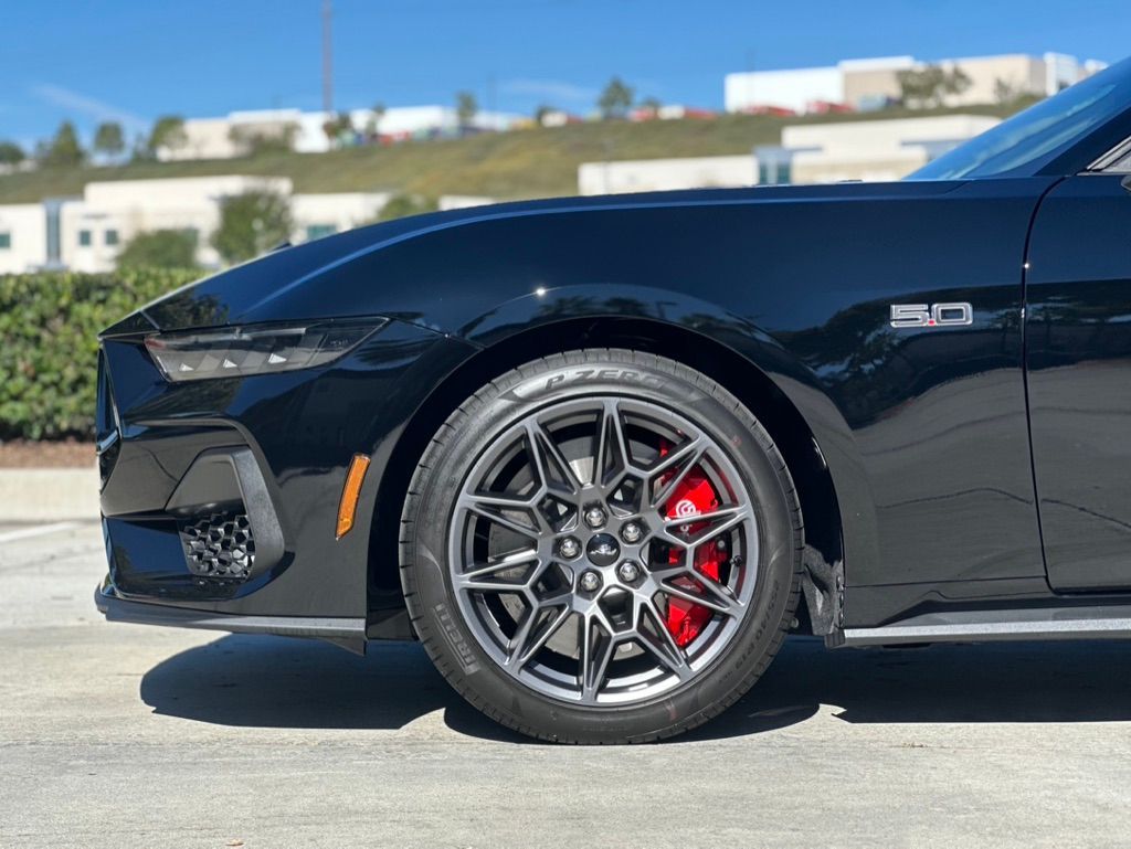Black Ford Mustang with dark gray wheels and red brake calipers, parked outside.