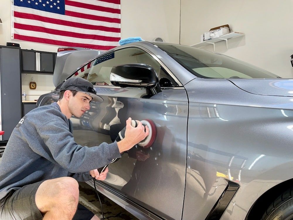 A man is polishing the side of a car in a garage.