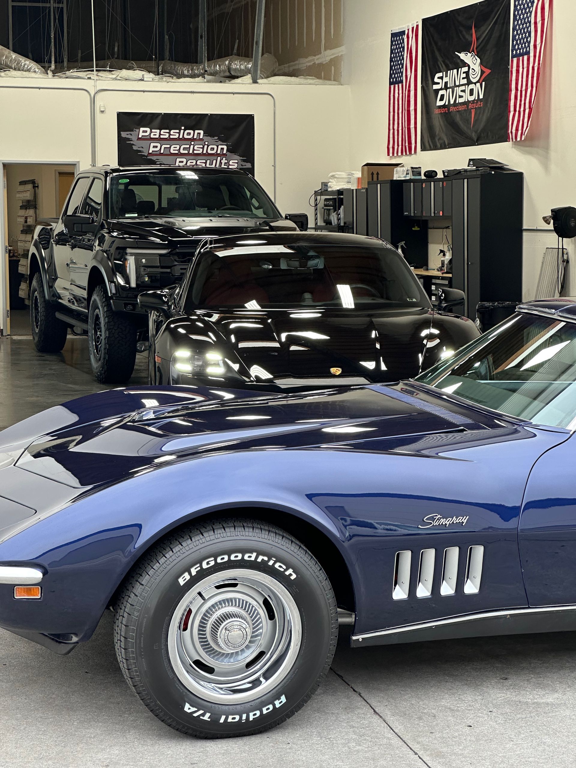 Blue Corvette, black sports car, and pickup truck in a garage.