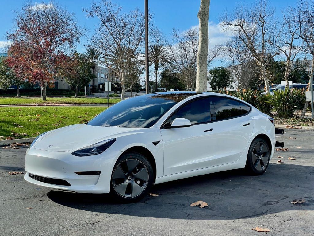 A white tesla model 3 is parked in a parking lot.