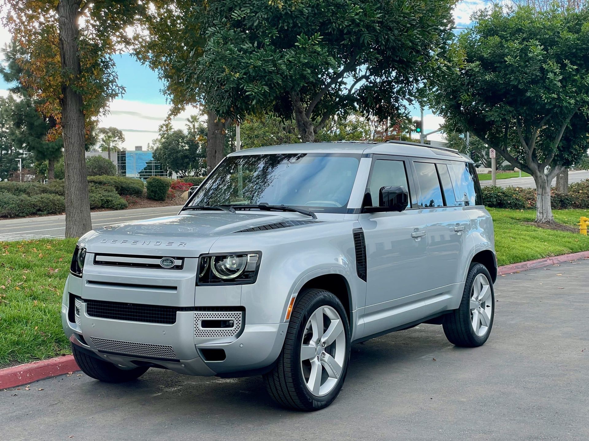 A silver land rover defender is parked in a parking lot.