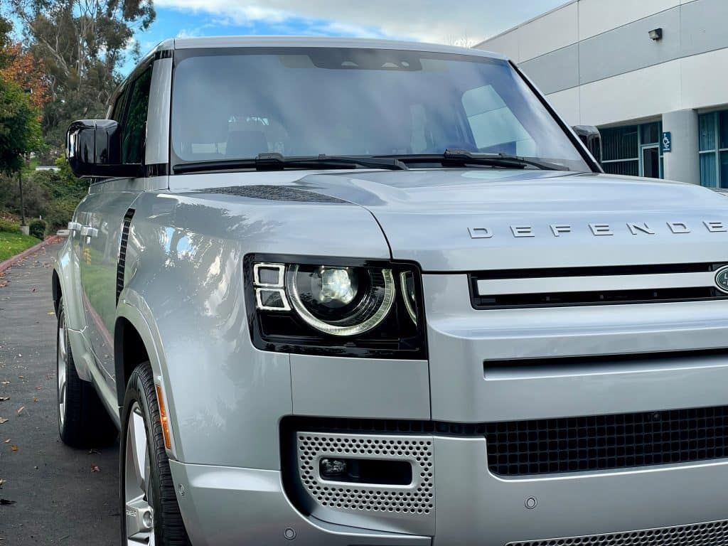 A silver land rover defender is parked in front of a building.