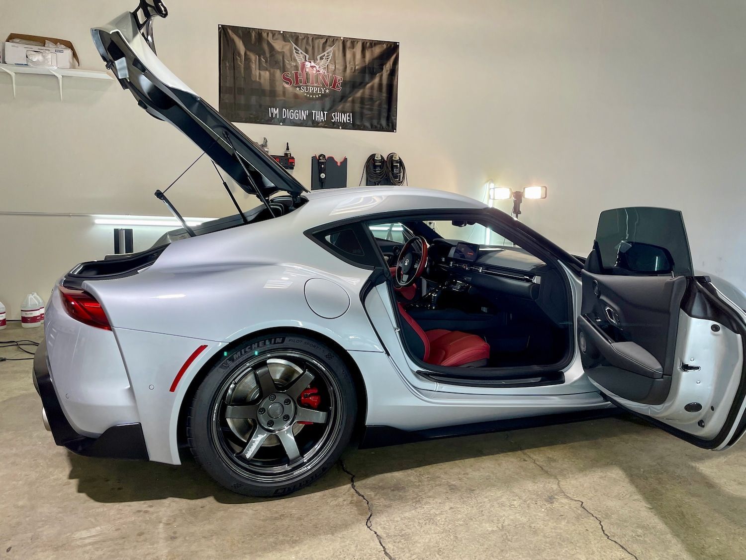 A white sports car with the trunk open is parked in a garage.
