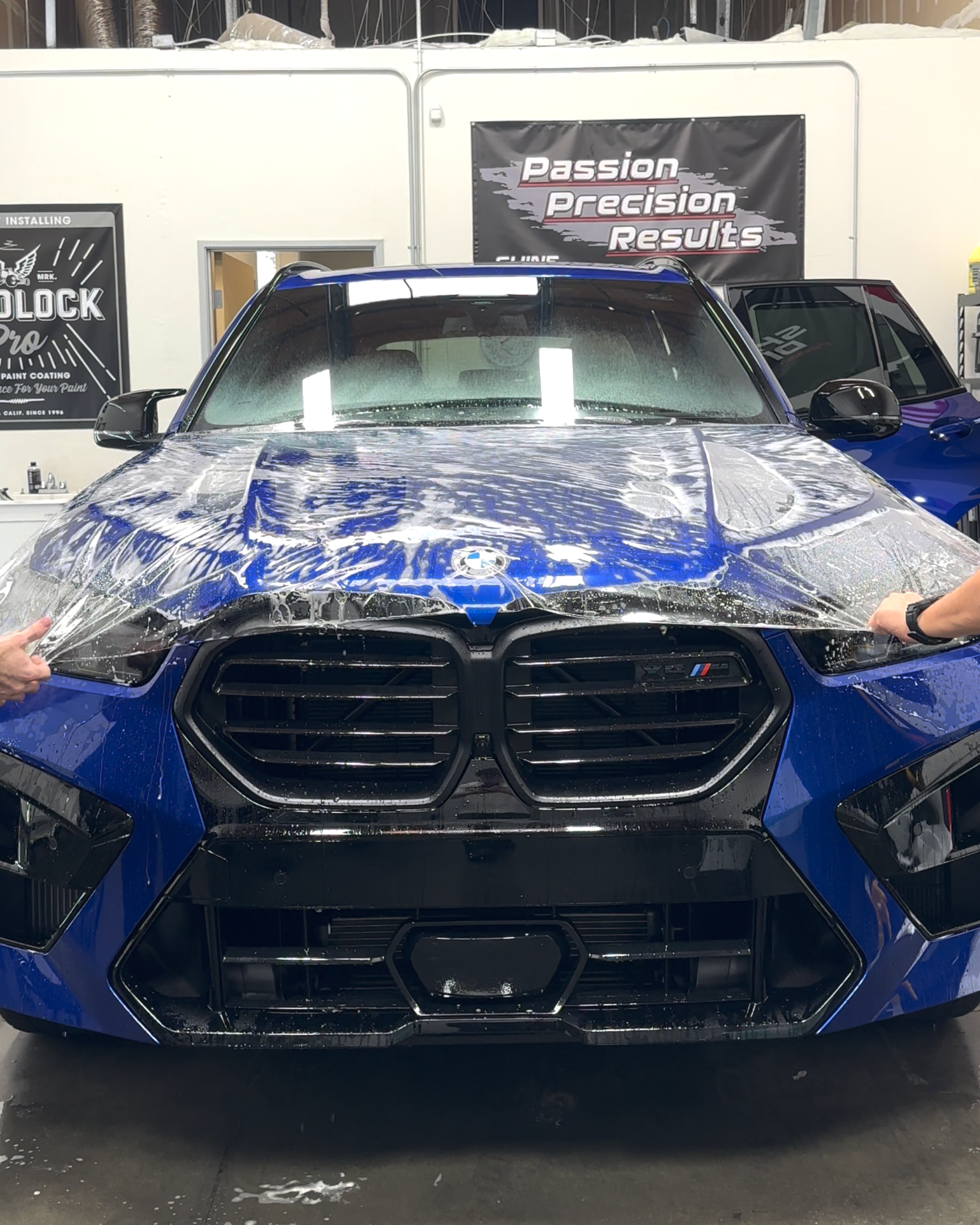 Blue BMW car being wrapped with protective film in a shop.