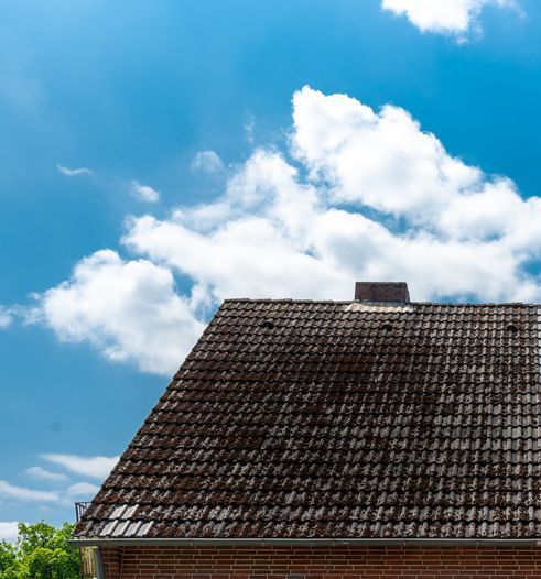 Old tiled roof under a bright blue sky with white clouds